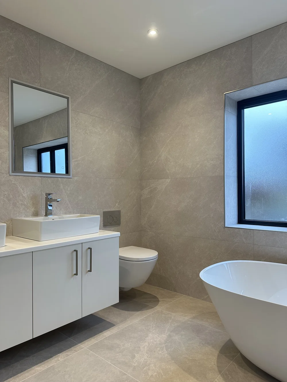 Contemporary stone-tiled bathroom with freestanding bath, floating vanity and twin basins — bathroom renovation Woking