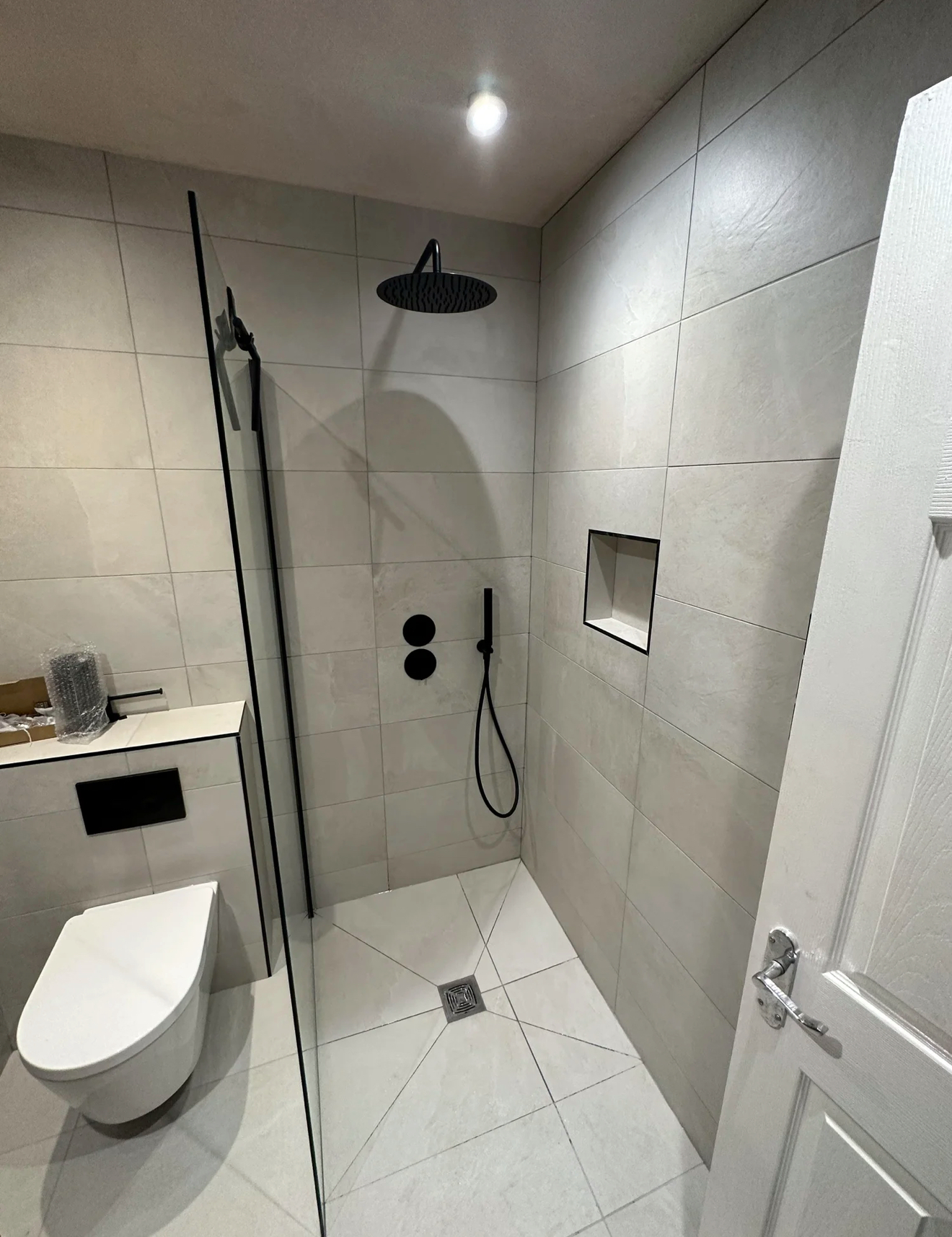 Compact shower room with matte black rainfall shower, wall-hung WC and recessed niche — bathroom installation Woking