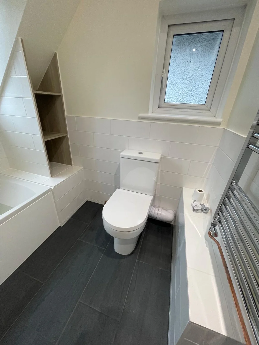 Loft bathroom with metro tiles, bespoke oak shelving and slate floor — bathroom installers Woking