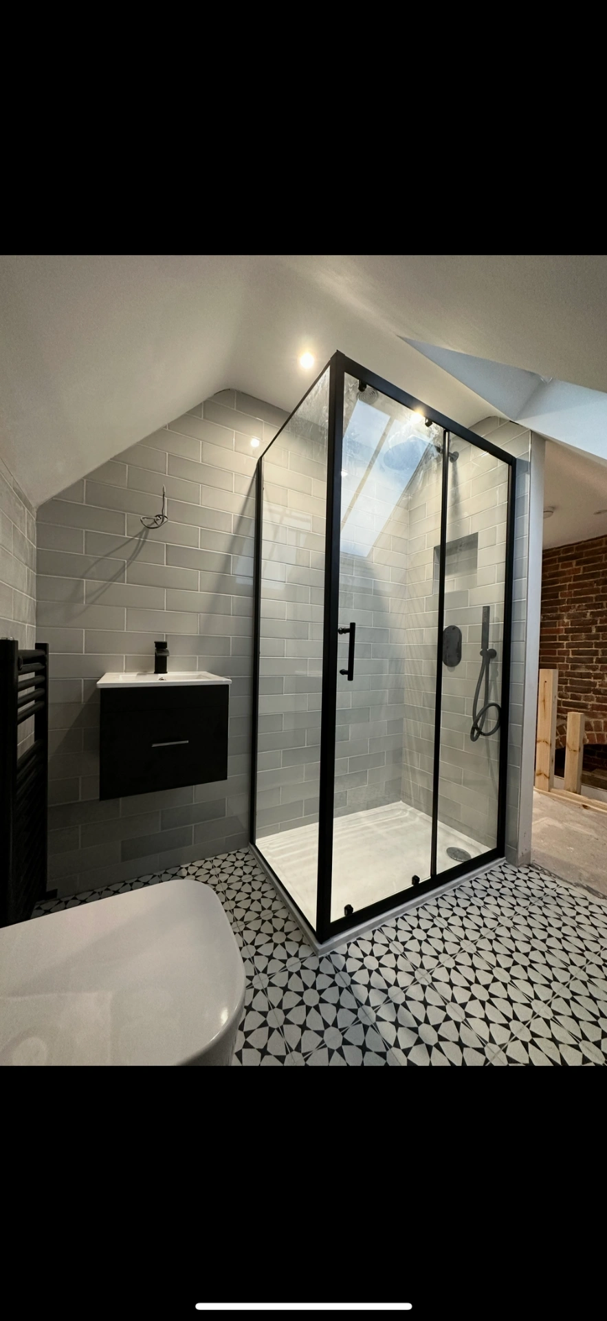 Loft ensuite with matte-black framed shower enclosure and patterned floor — Woking