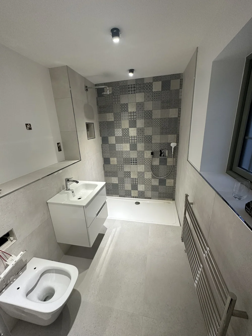 Modern shower room with patchwork feature tiles, white vanity and heated ladder rail — bathroom renovation Woking