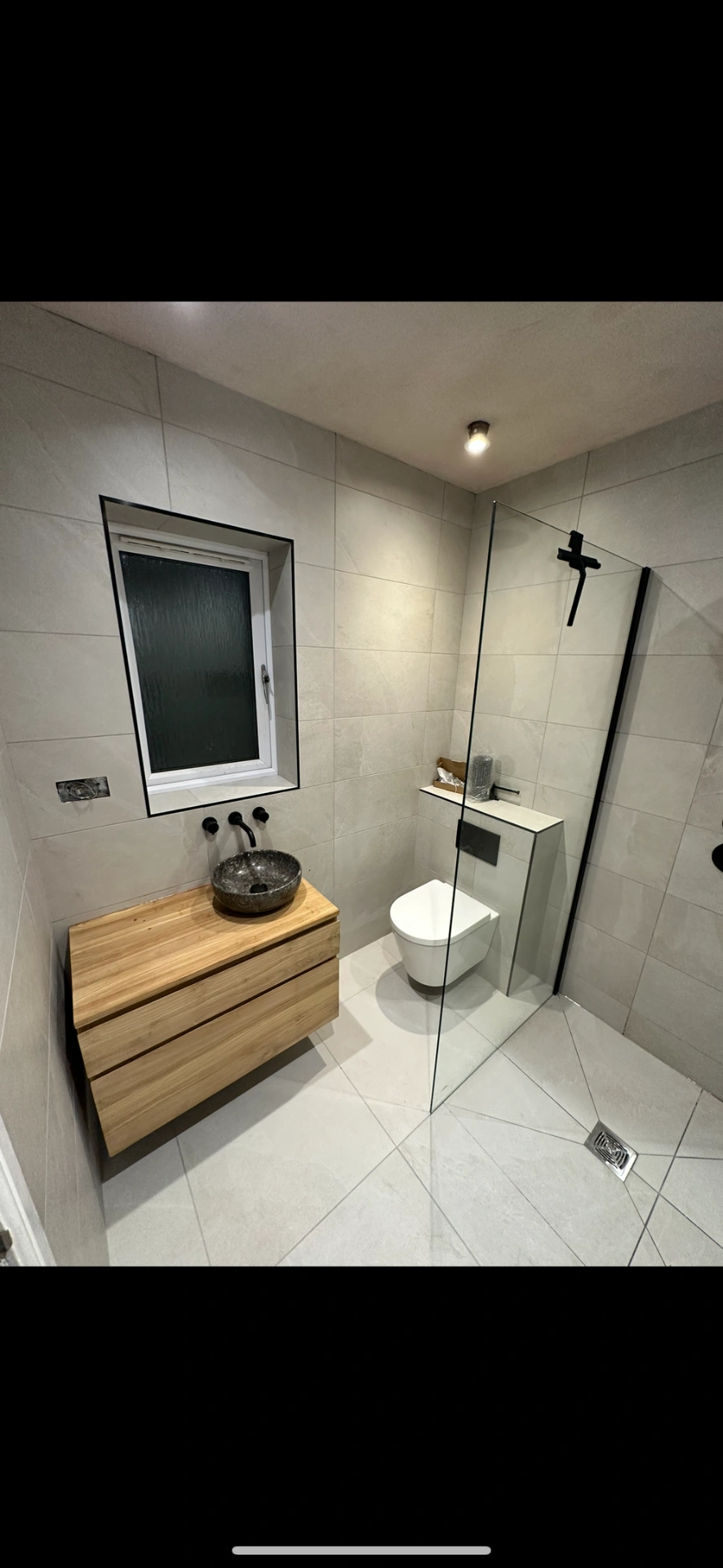Wet room with oak floating vanity, stone vessel basin and black-framed walk-in shower — wet room installation Woking