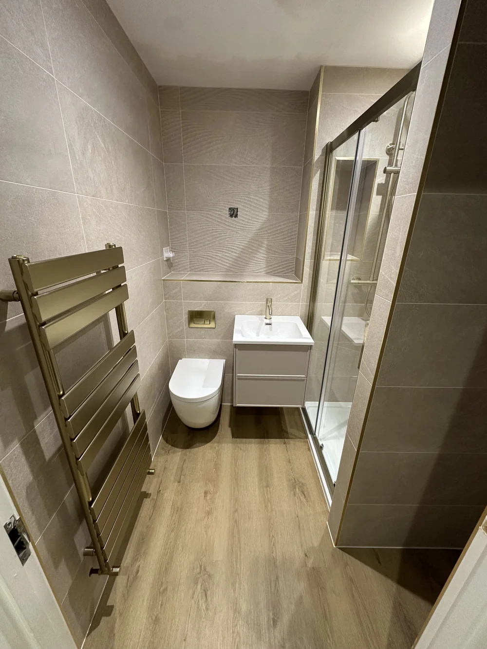 Modern shower room with brushed brass trim, sliding glass door and designer radiator — Woking bathroom fitters