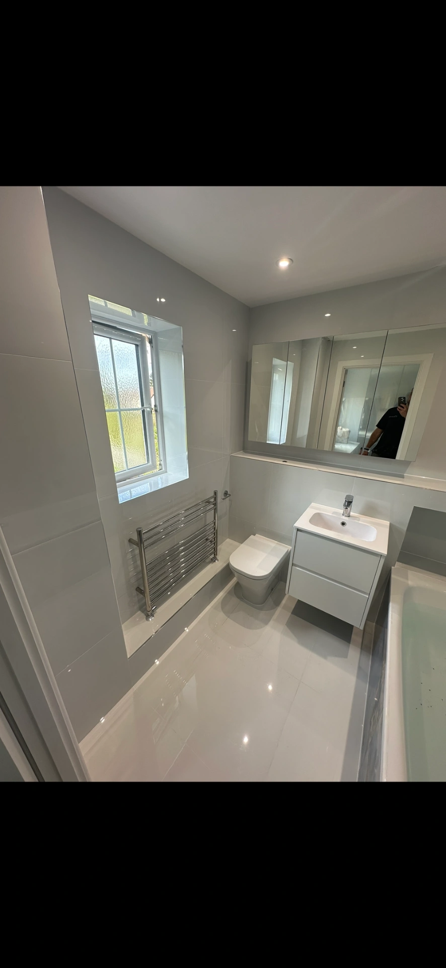 Bright white family bathroom with floating vanity, mirrored cabinet and gloss floor tiles — bathroom installation Woking