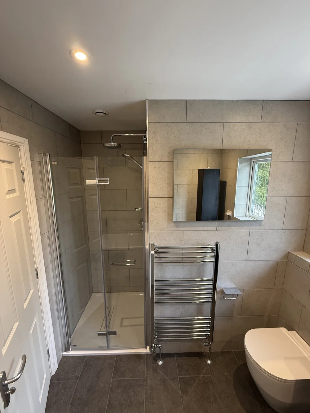 Stone-tiled family bathroom with hinged glass shower enclosure and chrome towel rail — bathroom installation Woking
