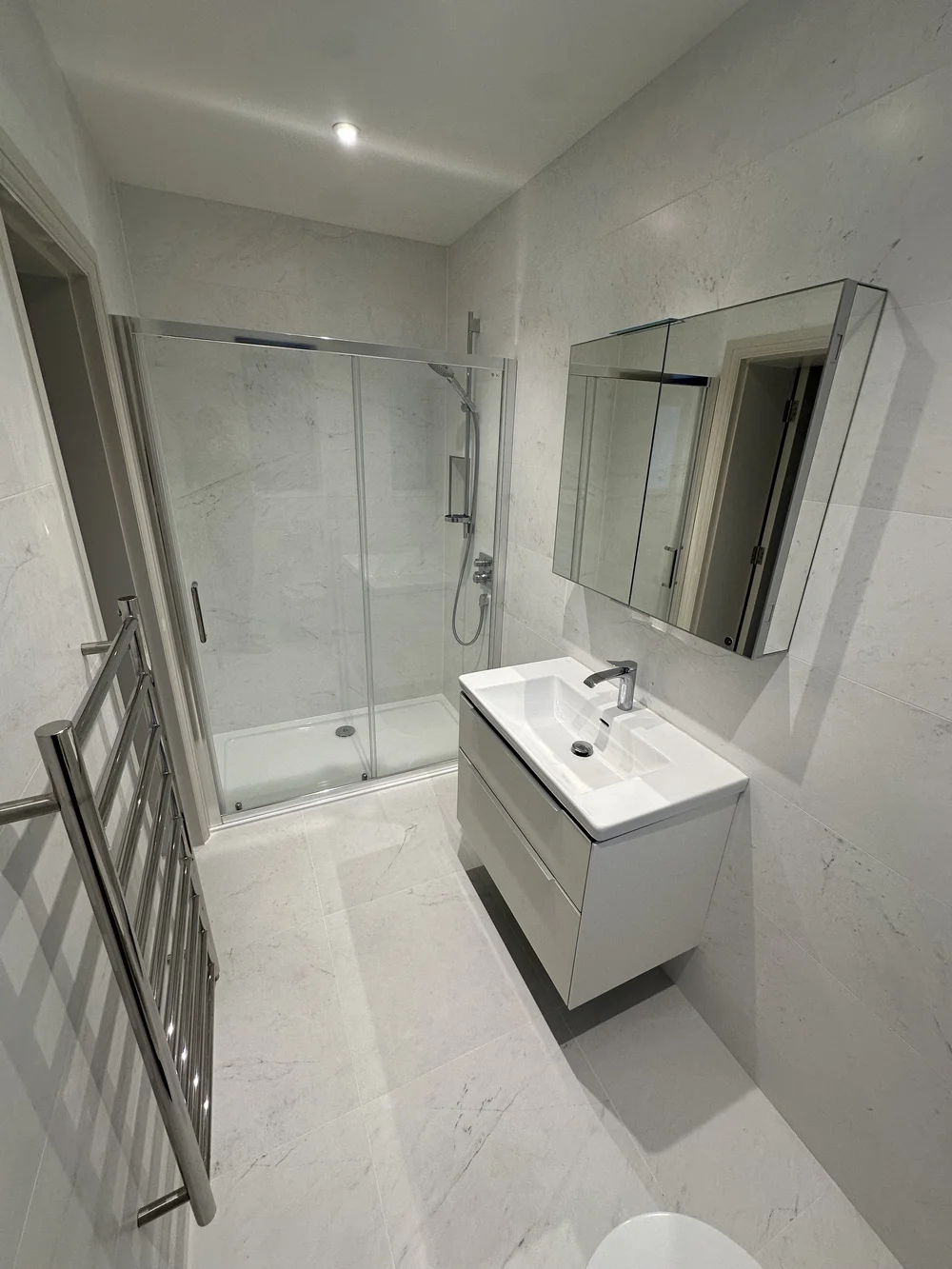 White marble shower room with sliding enclosure, wall-hung vanity and heated ladder rail — bathroom installation Woking