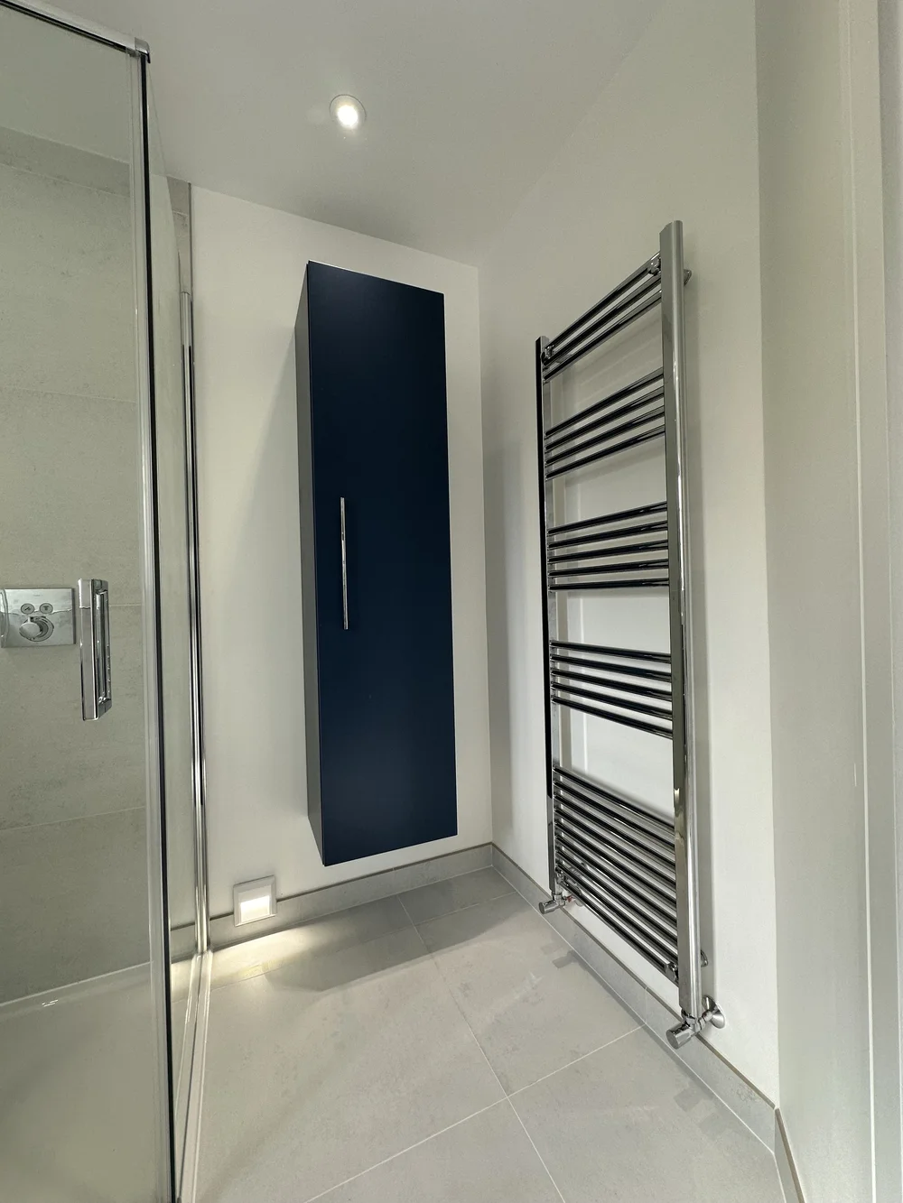 Detail of navy wall-hung storage cabinet with chrome ladder radiator — bathroom design Woking