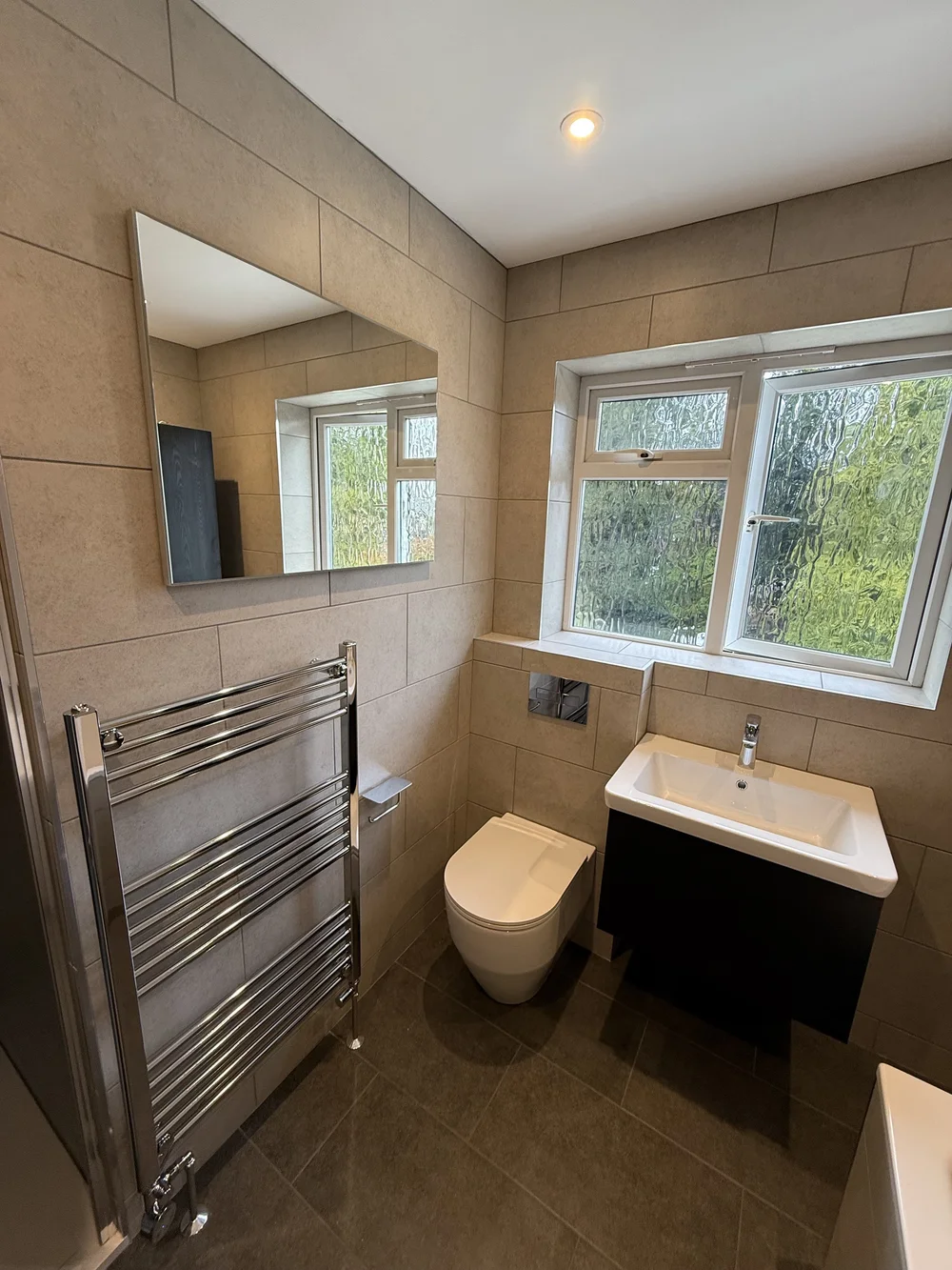 Beige-tiled bathroom with wall-hung black vanity and chrome heated rail — bathroom renovation Woking