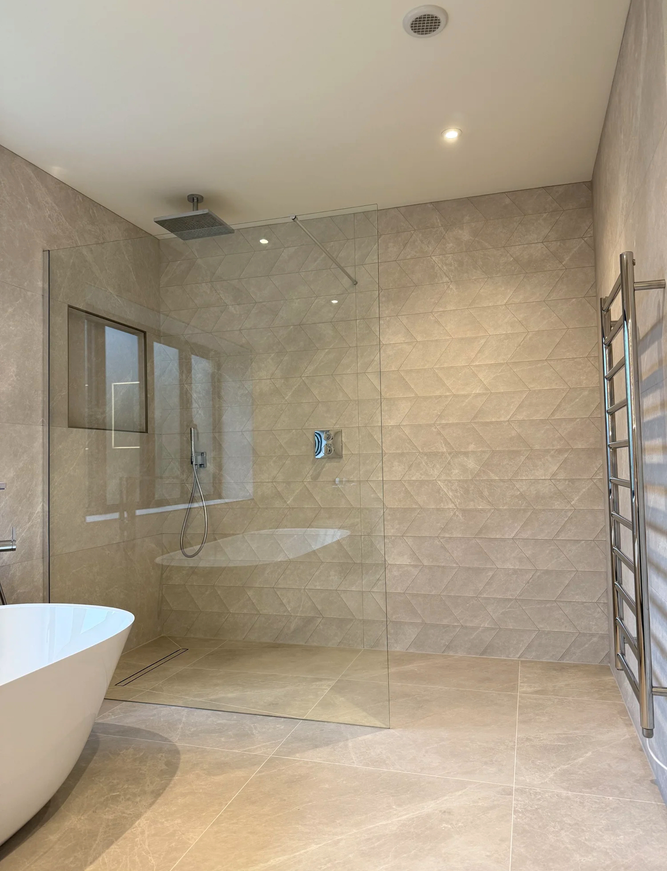 Stone-tiled wet room with freestanding bath, rainfall shower and chrome towel rail — bathroom installation Woking