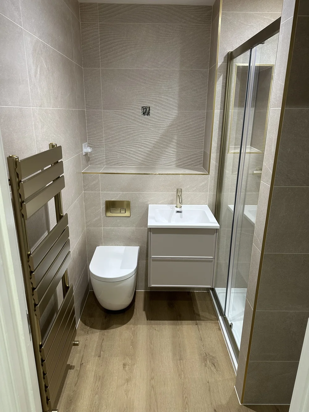 Textured stone shower room with brushed brass trim and designer towel rail — bathroom installation Woking