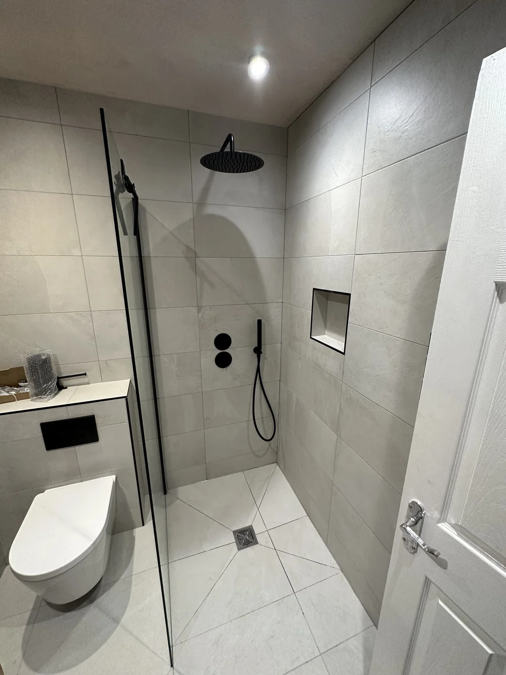 Stone-tiled walk-in shower with matte black rainfall head and recessed niche — wet room Woking