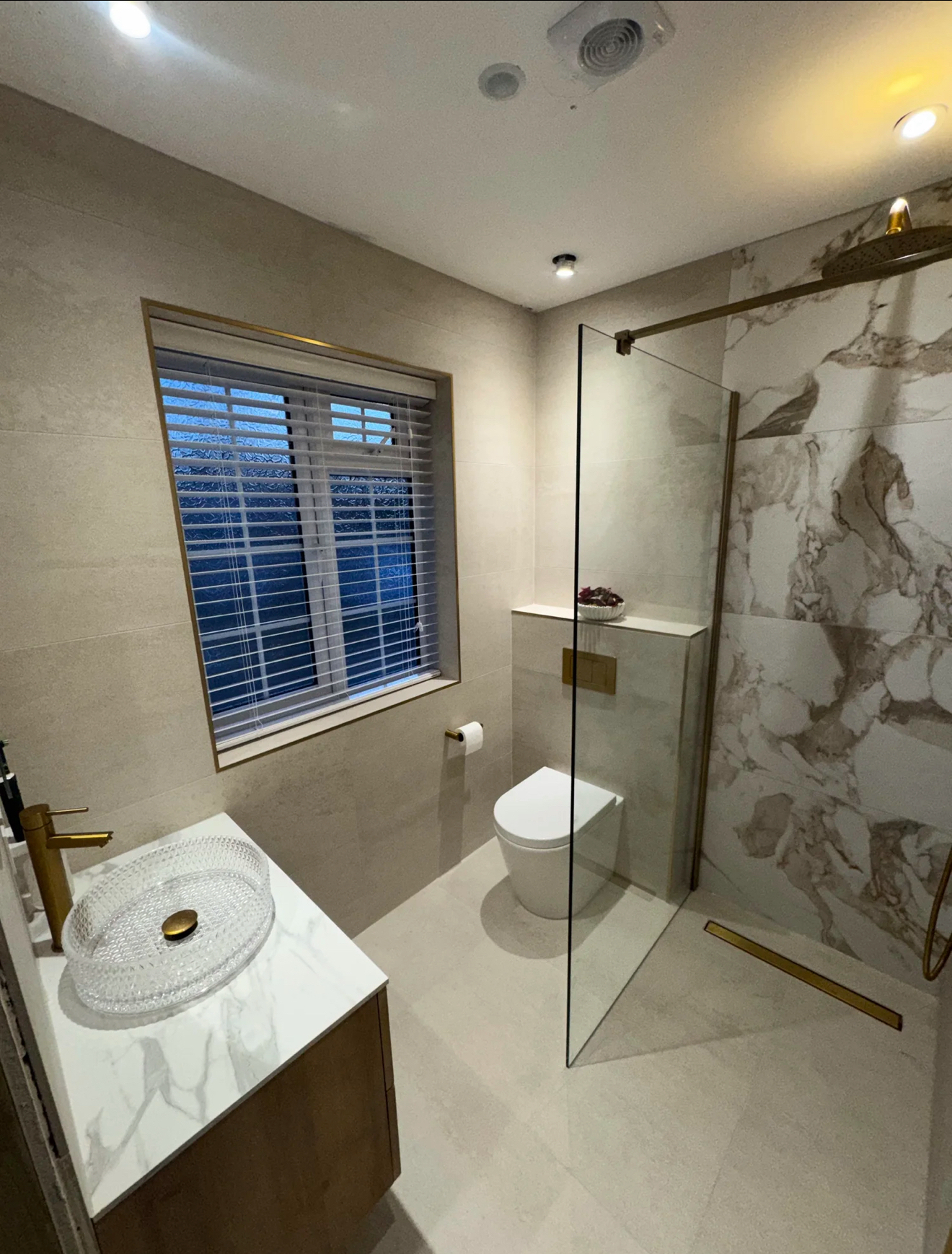 Marble and brass walk-in shower room with crystal basin and brushed gold fittings — luxury bathroom installation Woking
