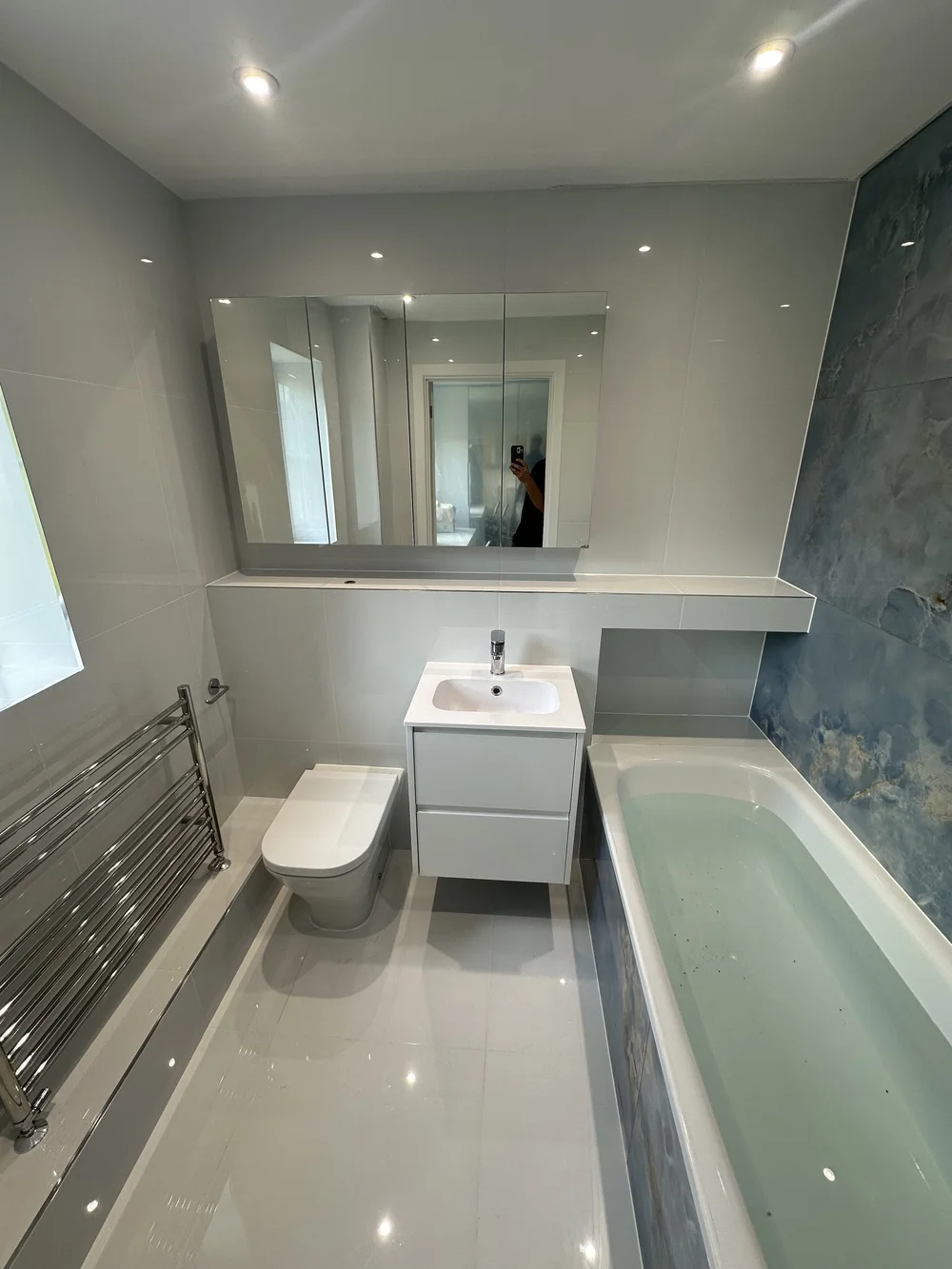 Bright family bathroom with mirrored cabinet, white vanity and blue onyx accent wall — bathroom renovation Woking
