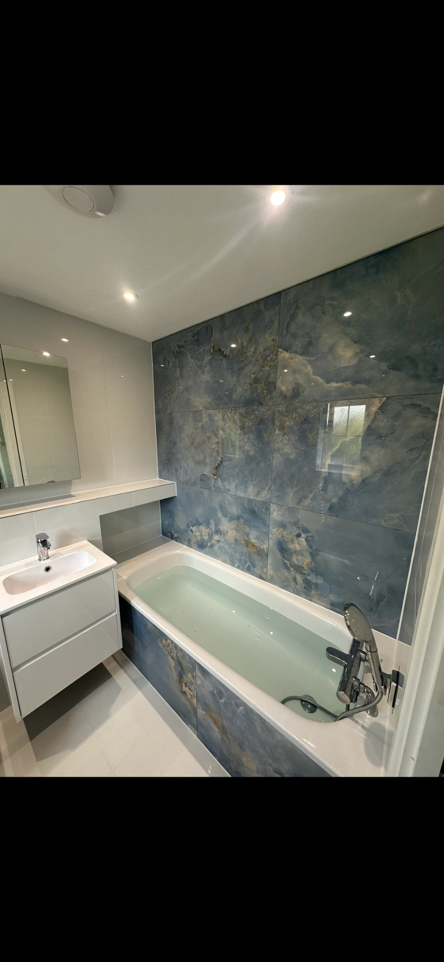 Bathroom with blue onyx-effect feature wall, panelled bath and floating white vanity — bathroom renovation Woking