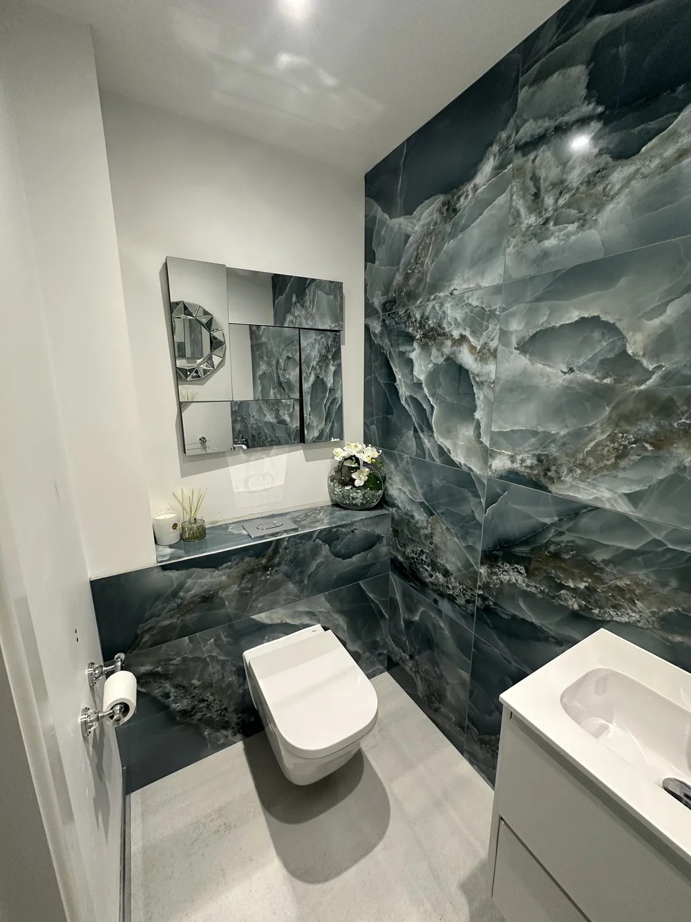 Bespoke cloakroom with full-height blue onyx feature wall and faceted mirror — bathroom design Woking