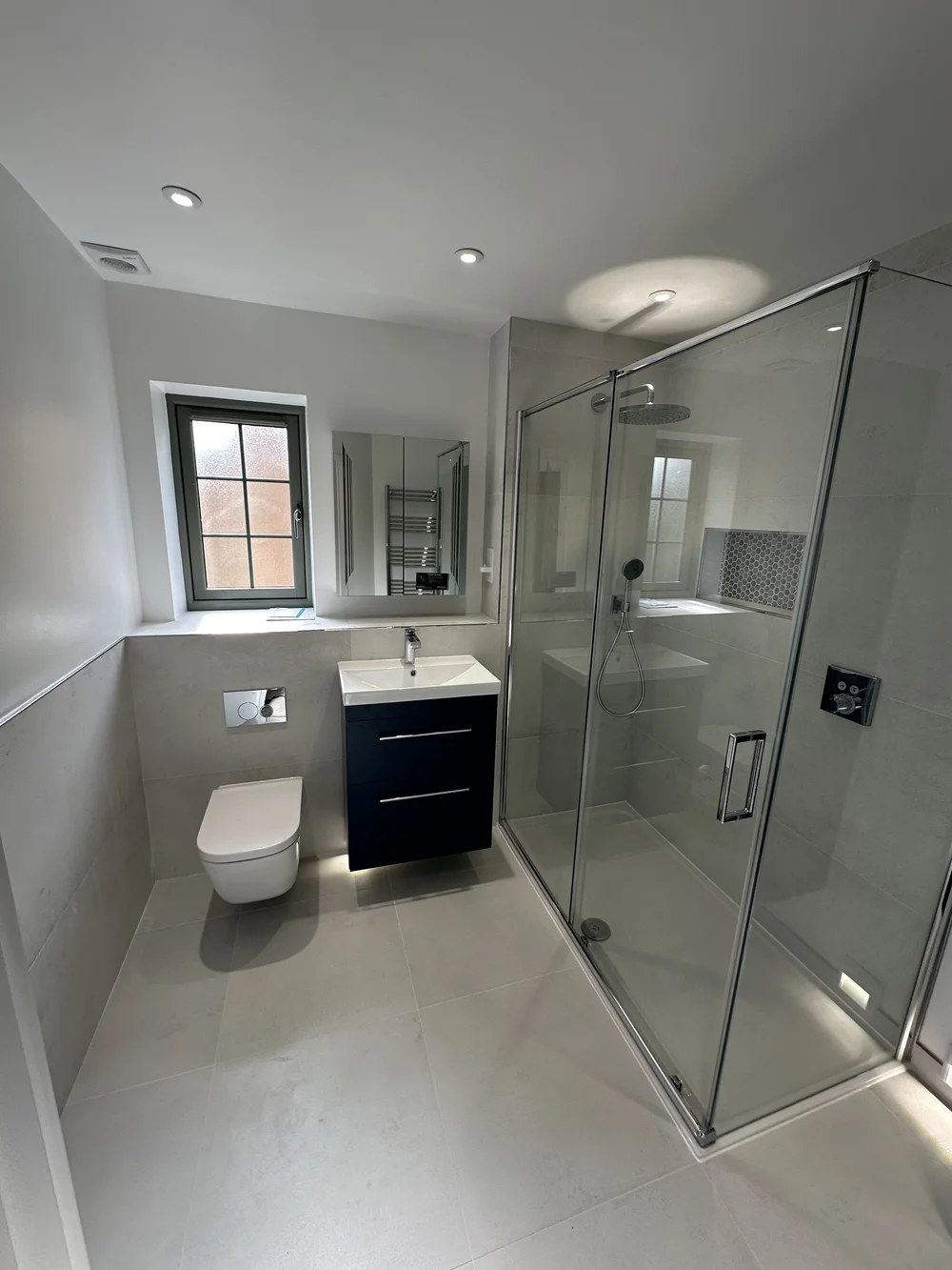 Fitted shower room with navy vanity, wall-hung WC and large glass shower enclosure — bathroom installation Woking