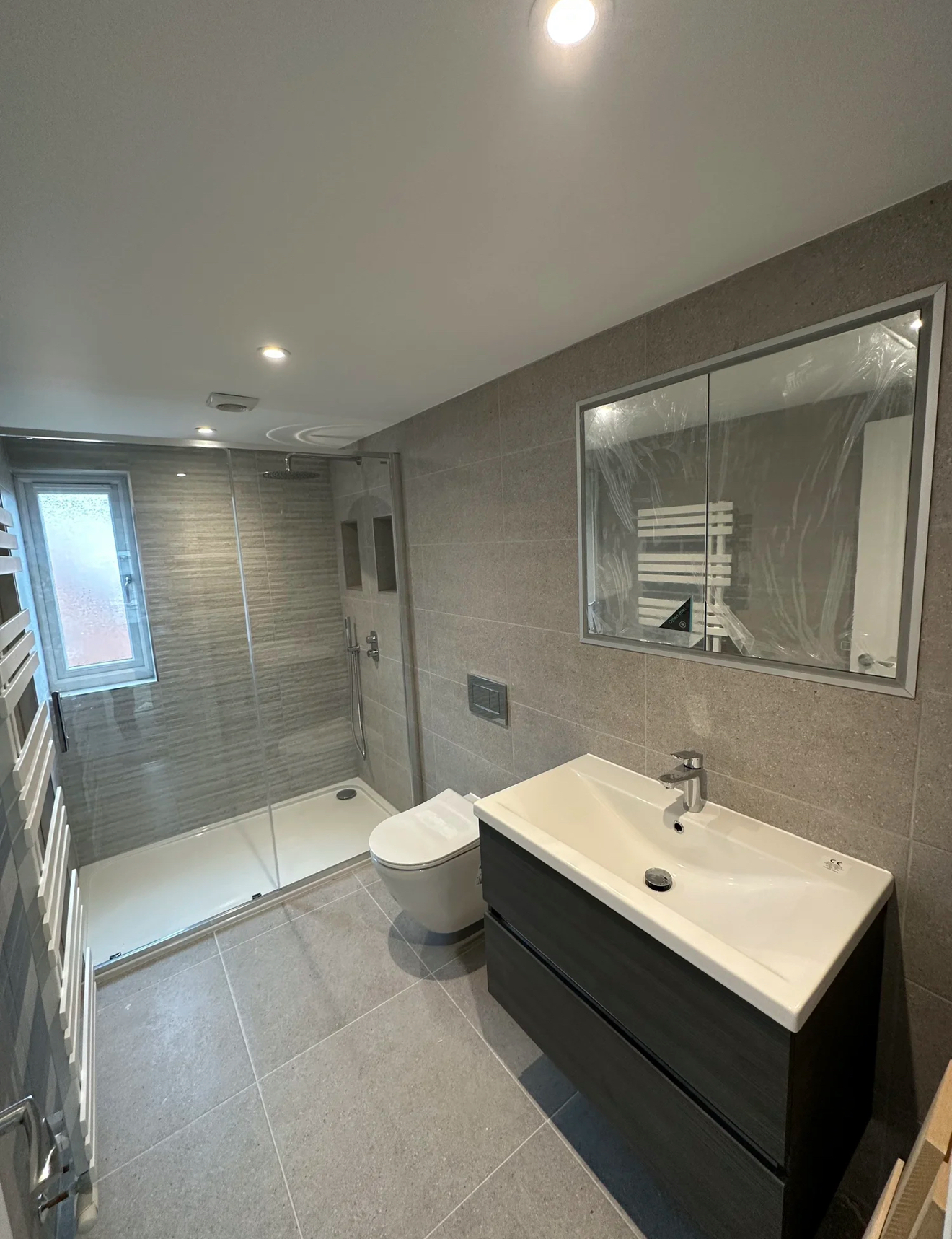 Grey-tiled shower room with sliding glass enclosure, mirrored cabinet and wall-hung vanity — bathroom renovation Woking