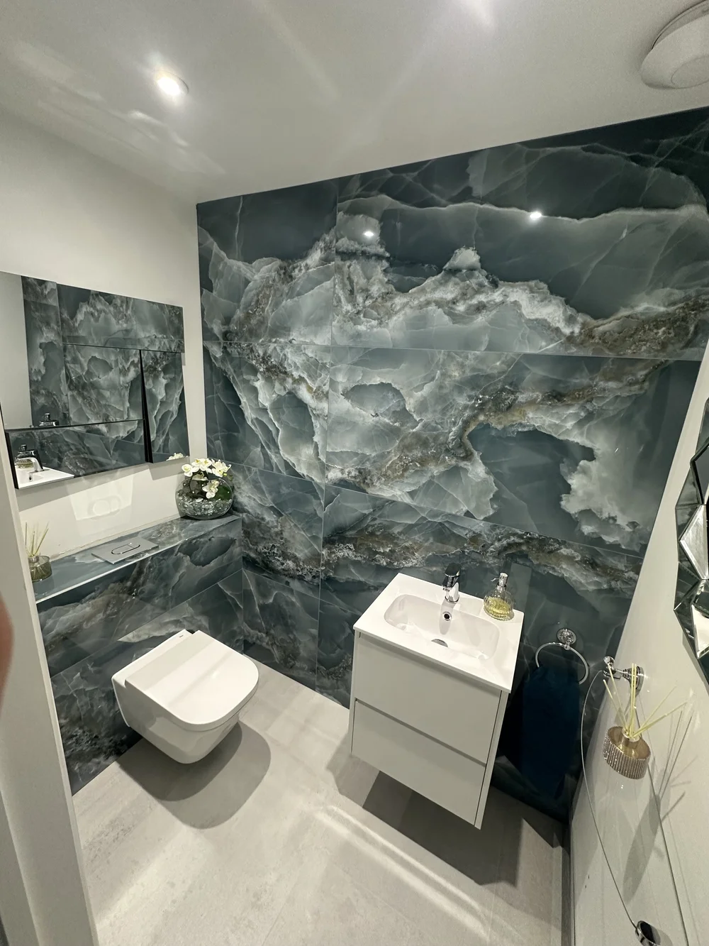 Cloakroom with blue onyx feature wall, wall-hung WC and floating white vanity — bathroom design Woking
