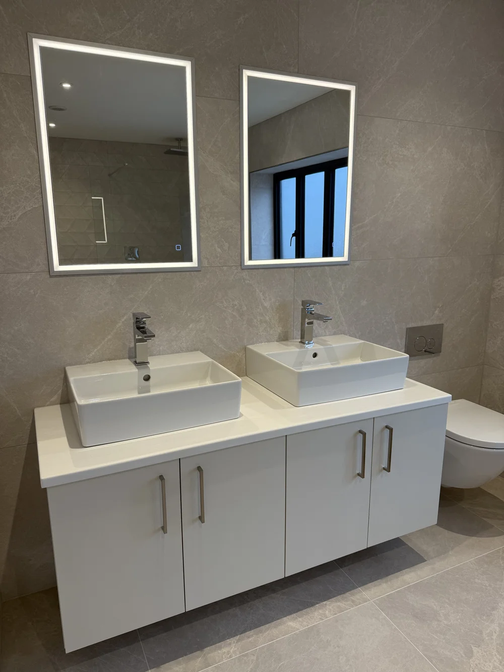 Twin countertop basins with LED mirrors on wall-hung vanity — ensuite installation Woking