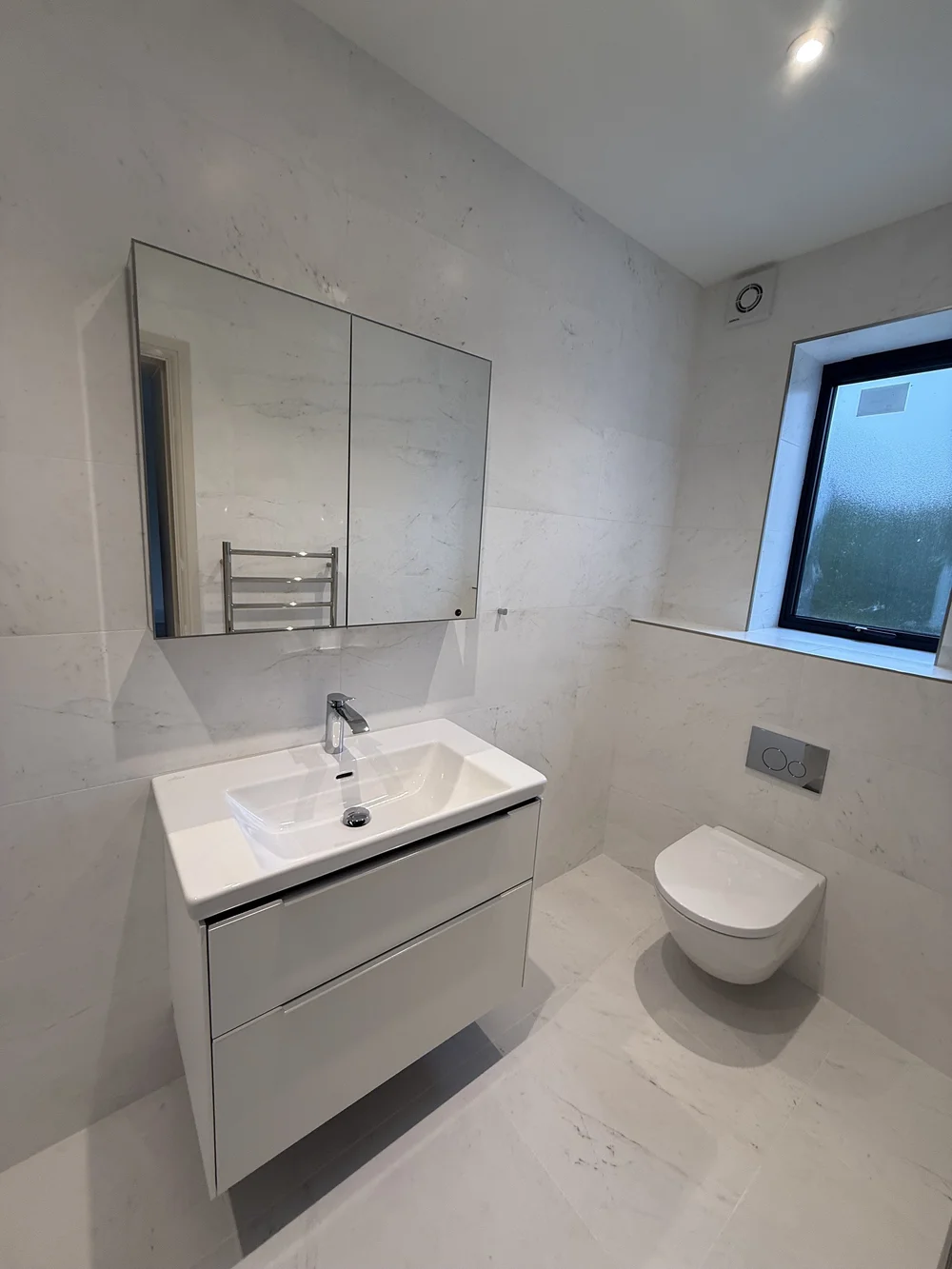 White marble family bathroom with wall-hung vanity and concealed cistern — Woking
