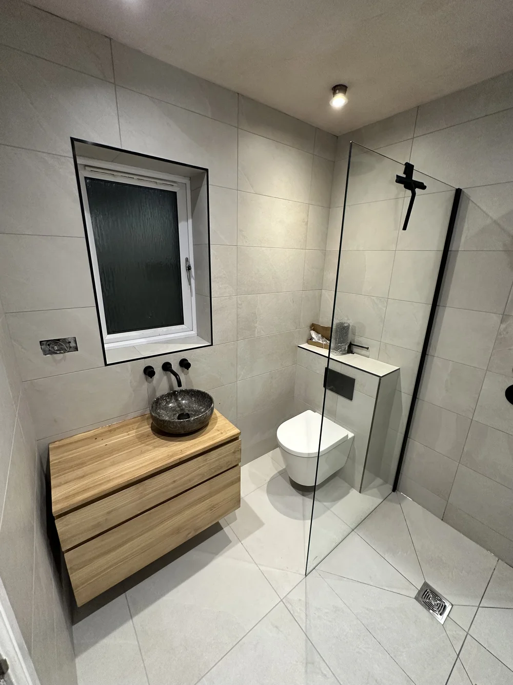 Wet room with oak floating vanity, stone basin and glass walk-in screen — wet room installation Woking