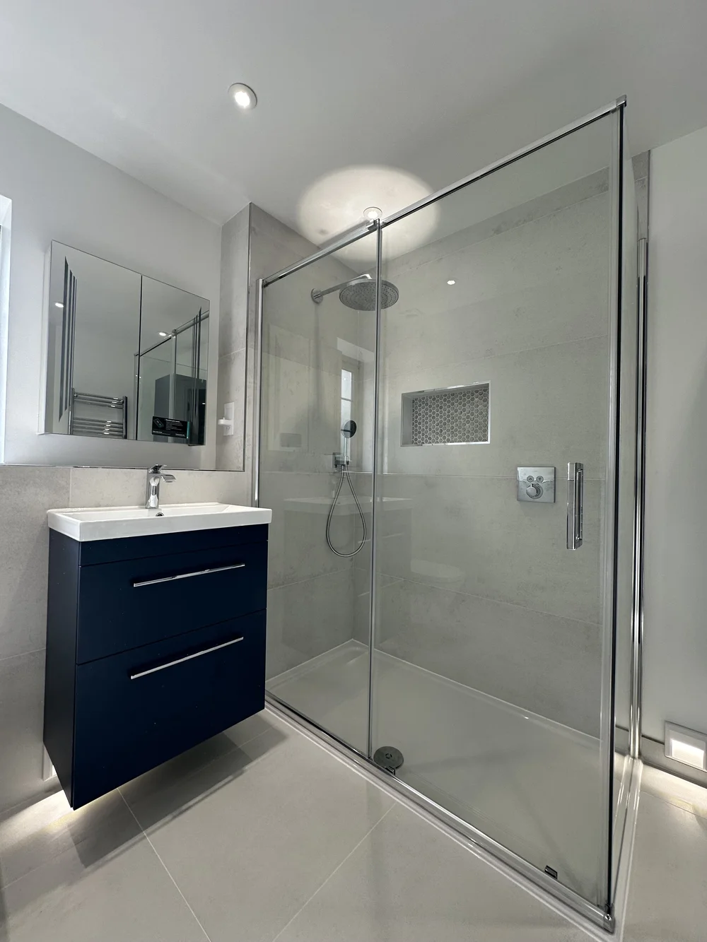 Modern ensuite with navy floating vanity, mirrored cabinet and sliding-door shower enclosure — bathroom installation Woking
