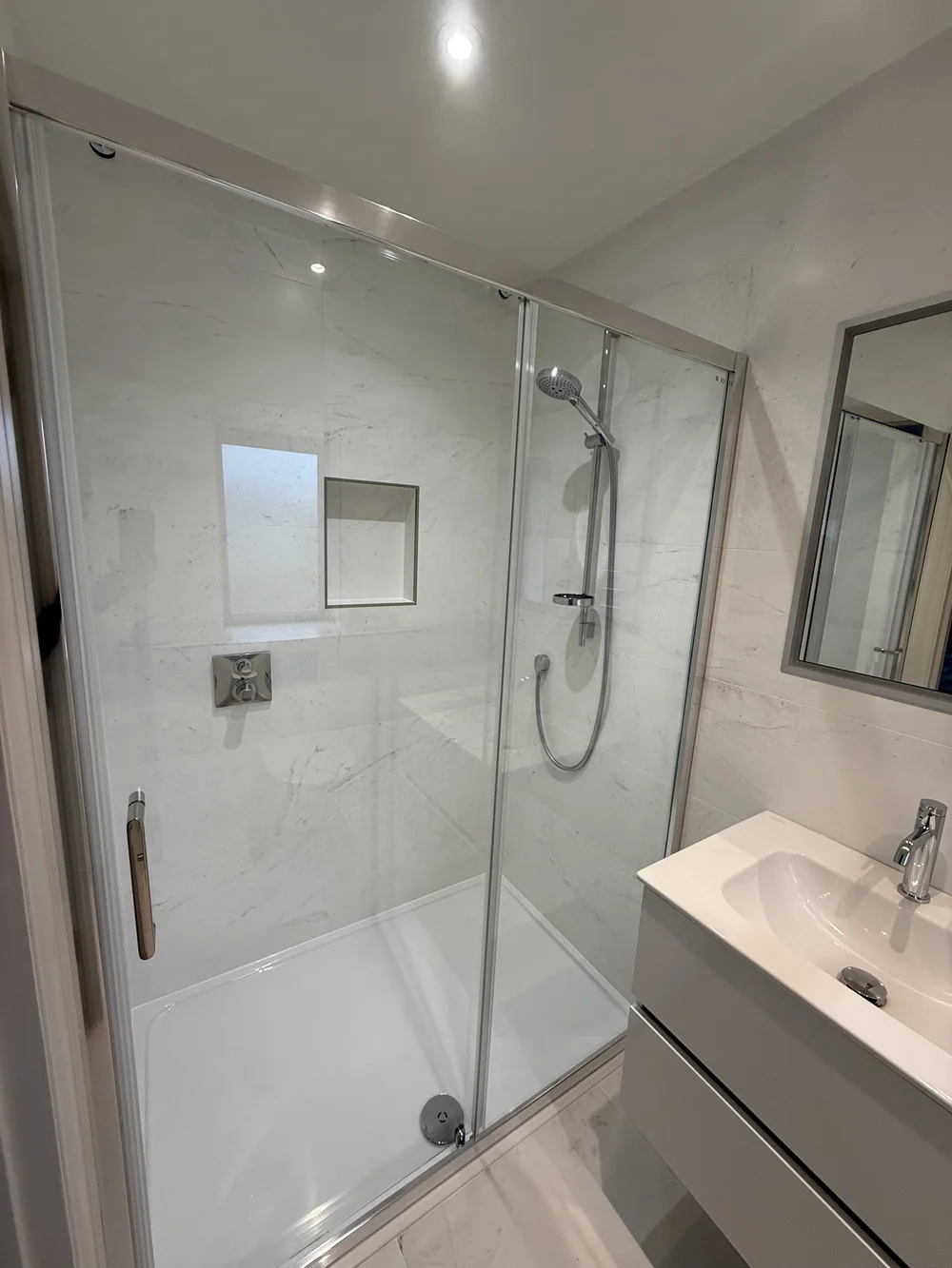 Marble shower enclosure with sliding door and recessed niche — bathroom renovation Woking
