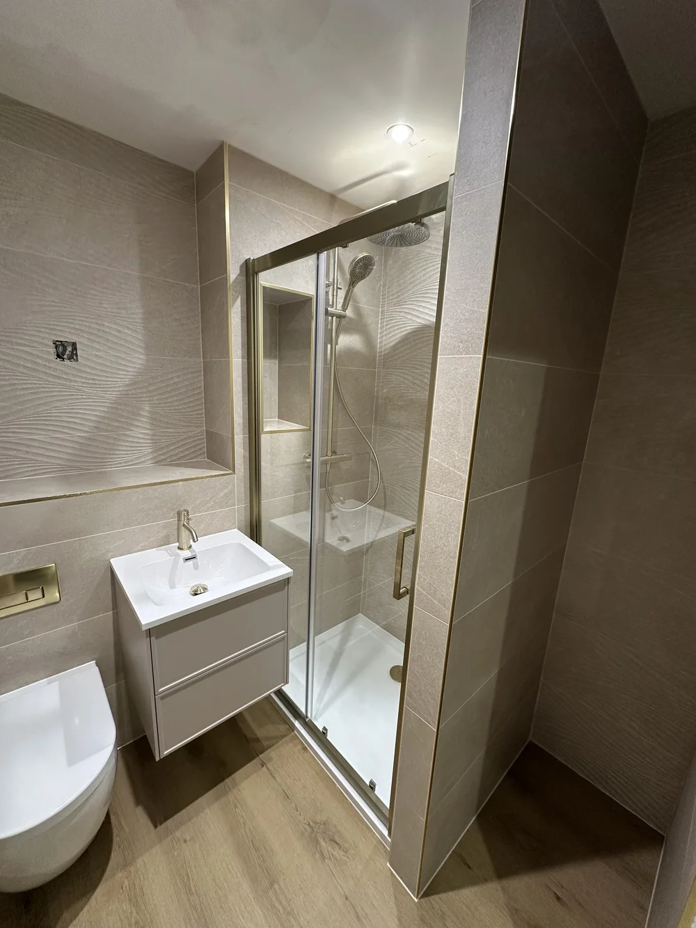 Wave-tiled shower room with brushed brass fittings and oak-effect floor — bathroom renovation Woking