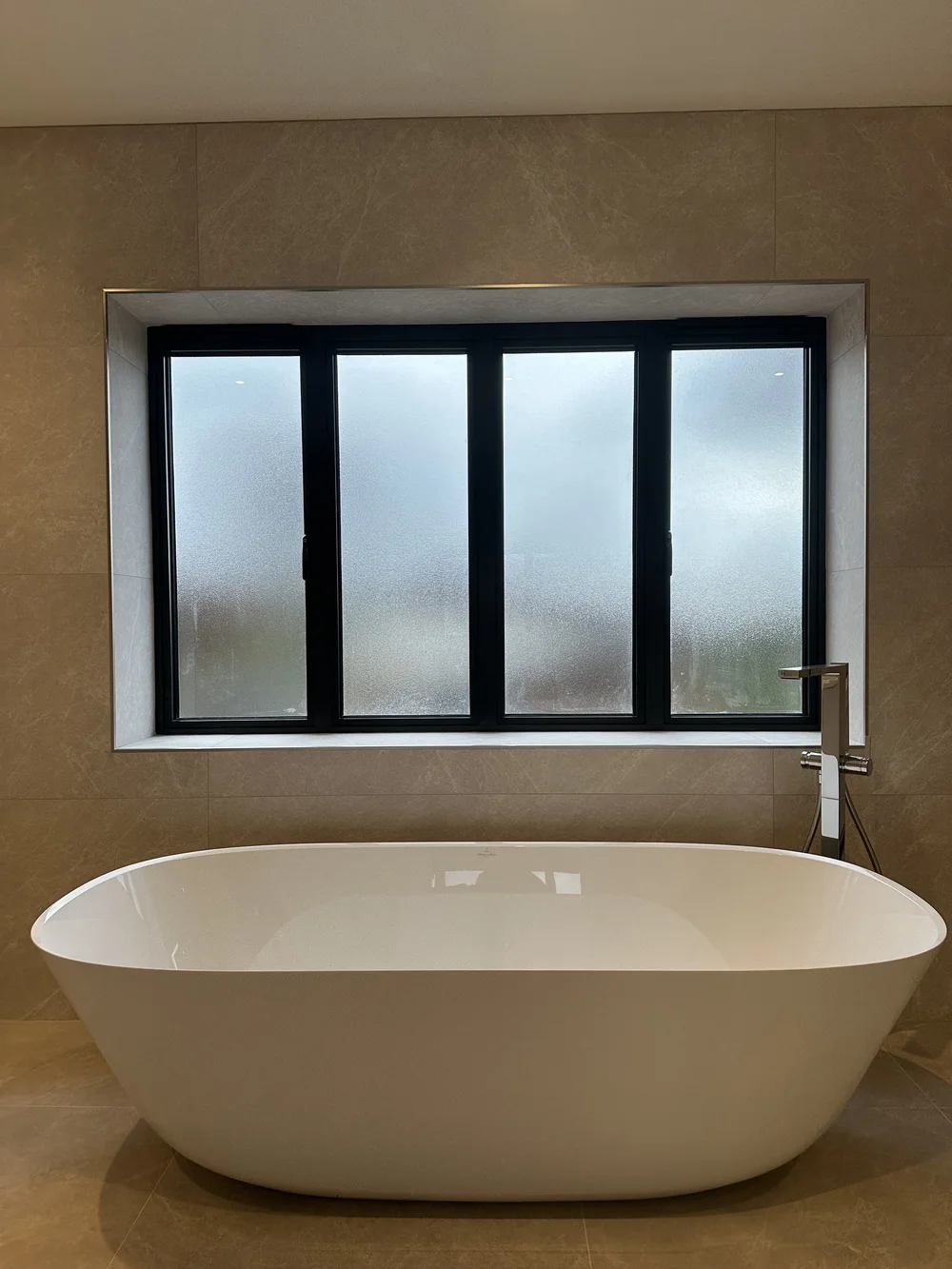 Freestanding stone-resin bath under crittall window in marble master bathroom — bathroom installation Woking